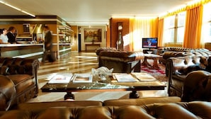 Een hotel lobby met leren banken, een salontafel met tijdschriften, een televisie en een receptiebalie met personeel.