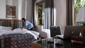 Een hotelkamer met een bed, een bureau met een laptop, een stoel en een raam met gordijnen.