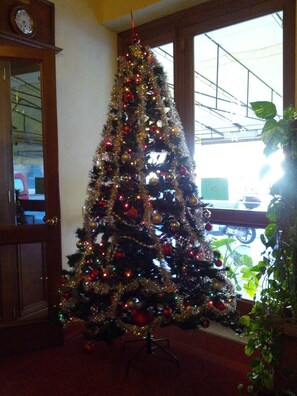 A Christmas tree with ornaments and lights, positioned near a window with a view of a parking garage. - Hotel Villa Kinzica (Pisa)