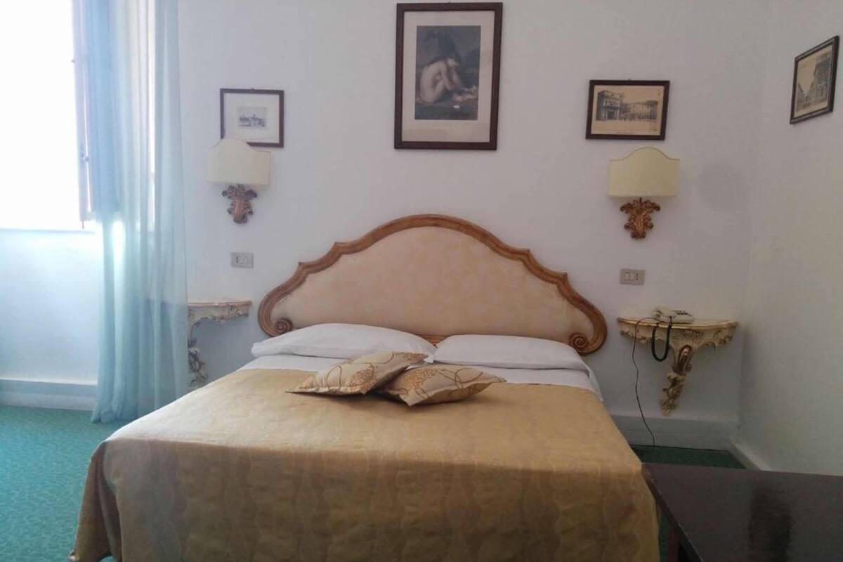 A hotel room with a large bed, two bedside lamps, a nightstand, and framed pictures on the wall.