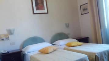 Una habitación de hotel con dos camas individuales, cada una con una almohada y una mesita de noche. Encima de las camas, hay un cuadro en la pared.