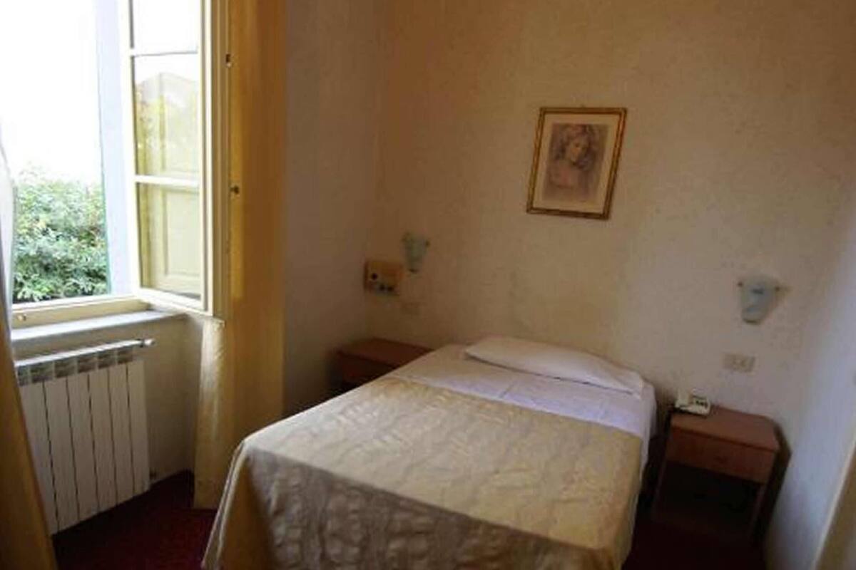 A room with a bed, a window with curtains, a radiator, and a small bedside table.