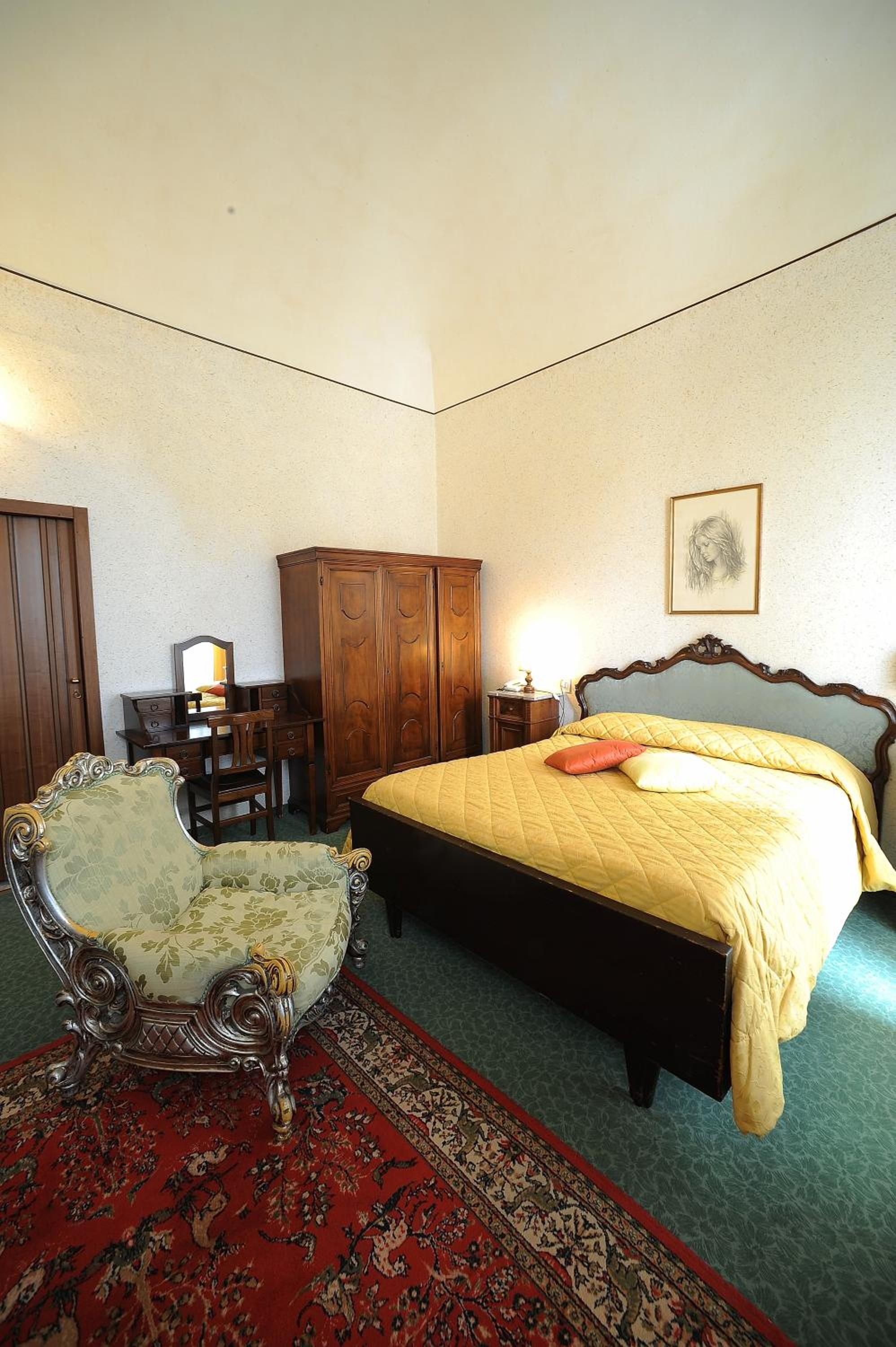 A bedroom with a bed, a wooden wardrobe, a desk with a chair, and a patterned rug.