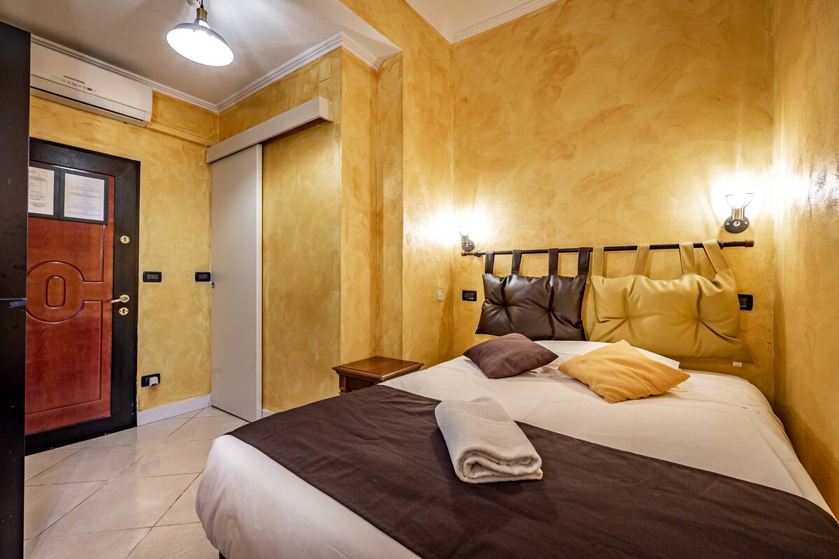 Una habitación de hotel con una cama grande, una puerta de madera y una lámpara en el techo.