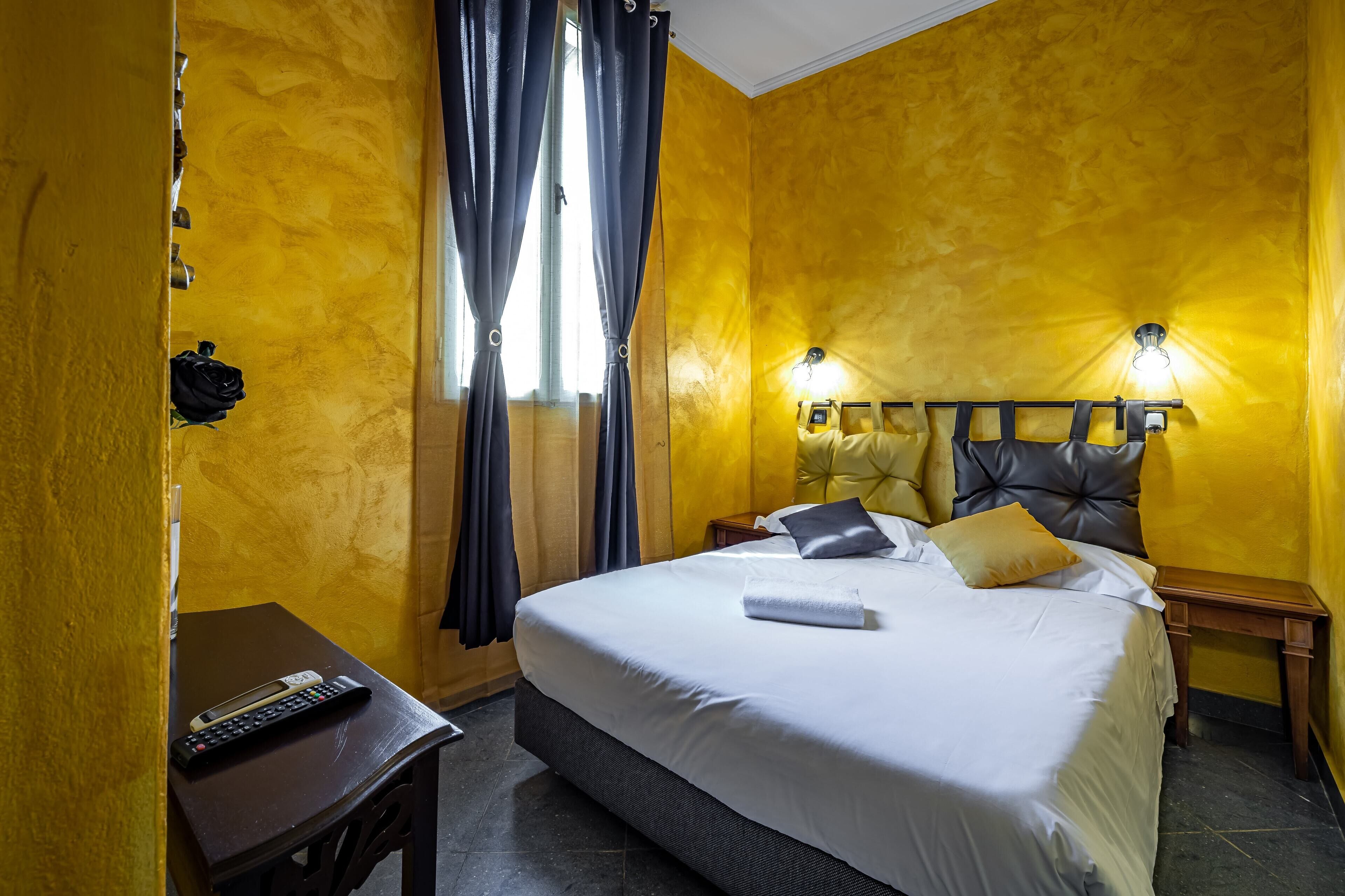 A hotel room with a large bed, a bedside table with a remote control, and a nightstand with a lamp.