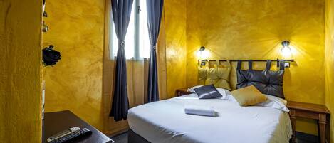 A hotel room with a large bed, a bedside table with a remote control, and a nightstand with a lamp.