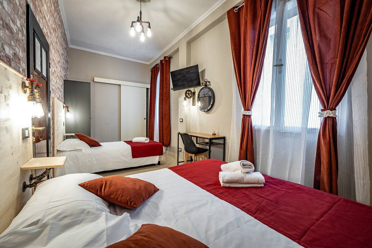 Habitación de hotel con dos camas, un escritorio, una silla, un televisor y un espejo.