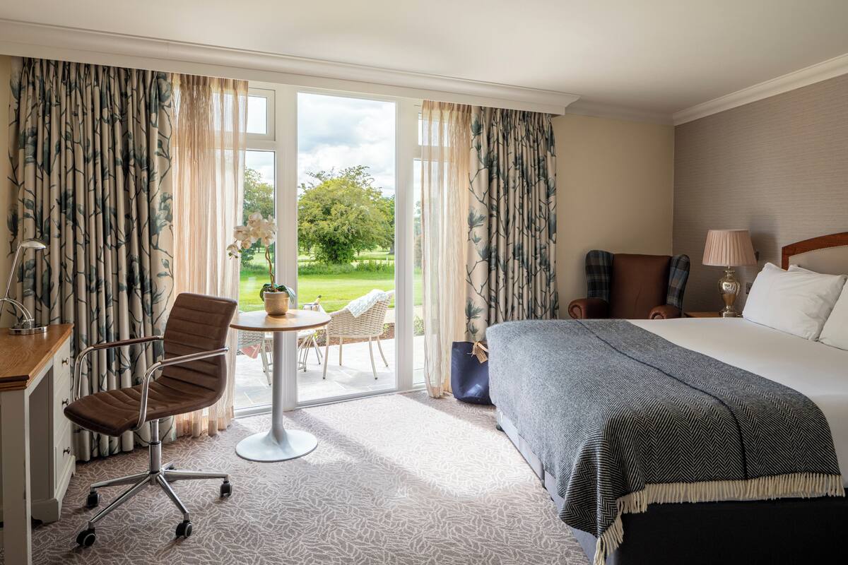 Ein Hotelzimmer mit Bett, Schreibtisch, Stuhl, einem kleinen Tisch und Blick ins Freie.