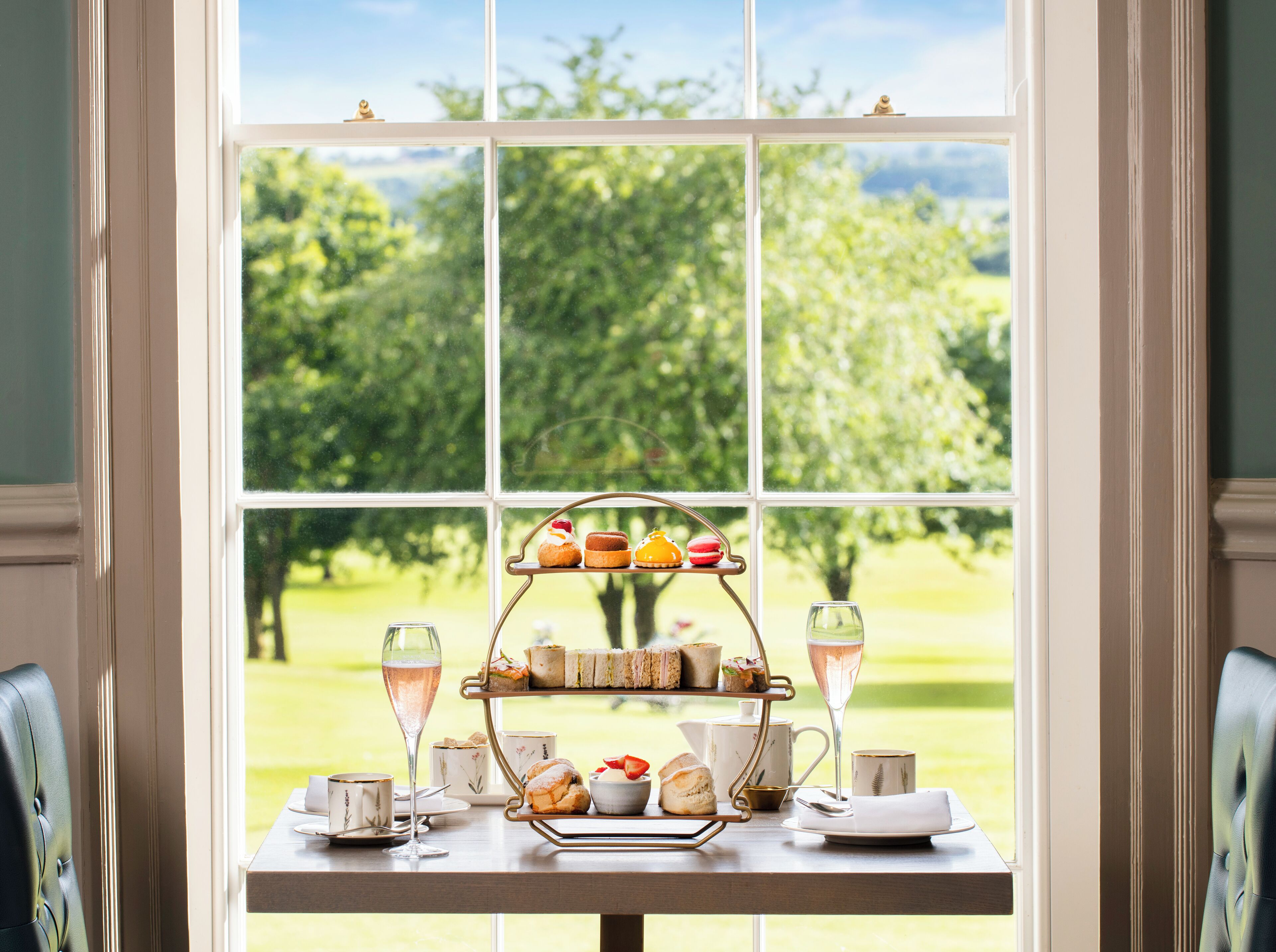 Una mesa preparada para servir té, con vista a un jardín exuberante a través de un ventanal grande.