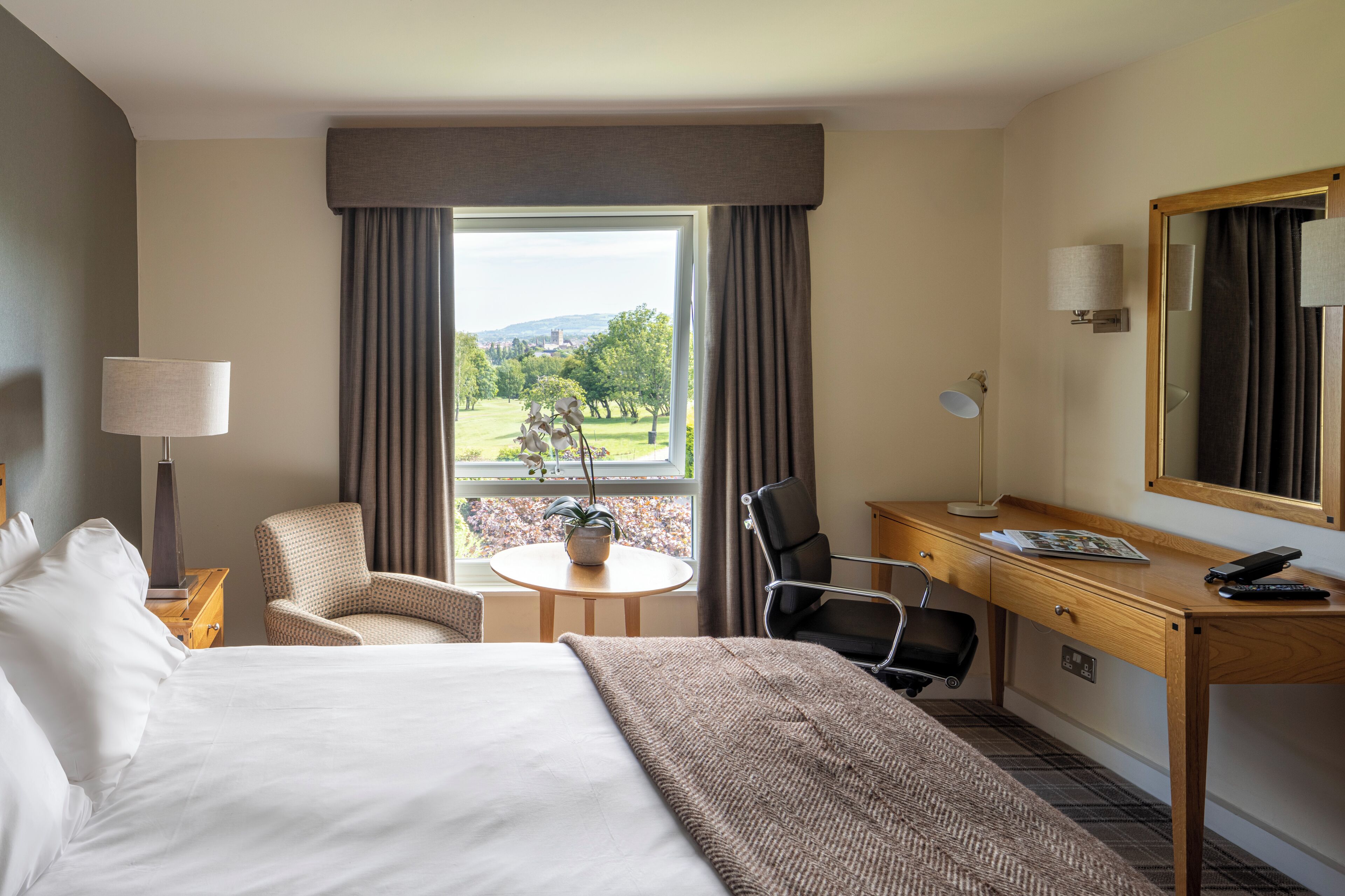Une chambre d’hôtel équipée d’un lit, d’un bureau, d’une chaise, d’une lampe et offrant une vue sur le paysage.