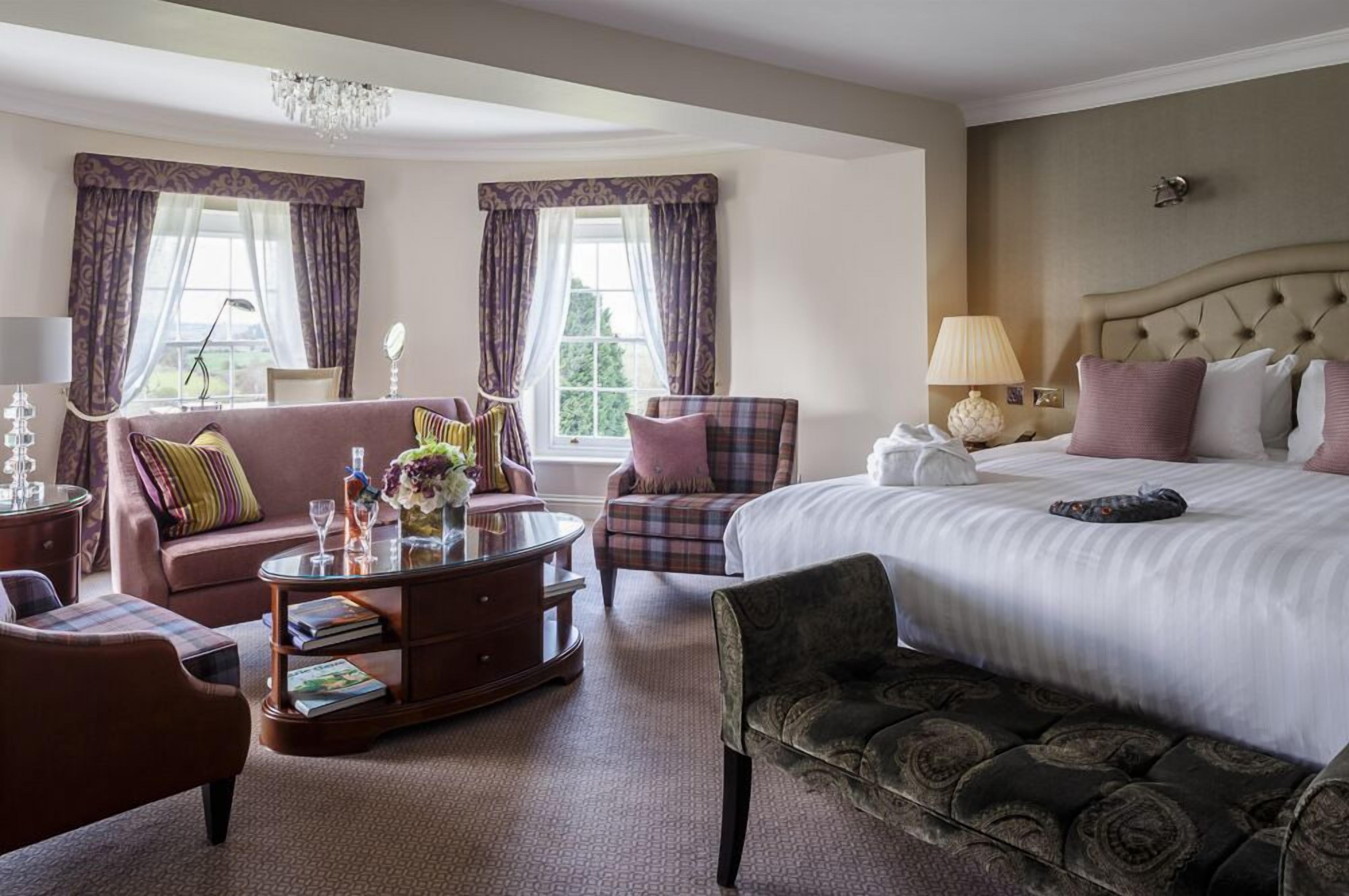 A hotel room with a large bed, a sofa, a chair, a coffee table, and a chandelier.