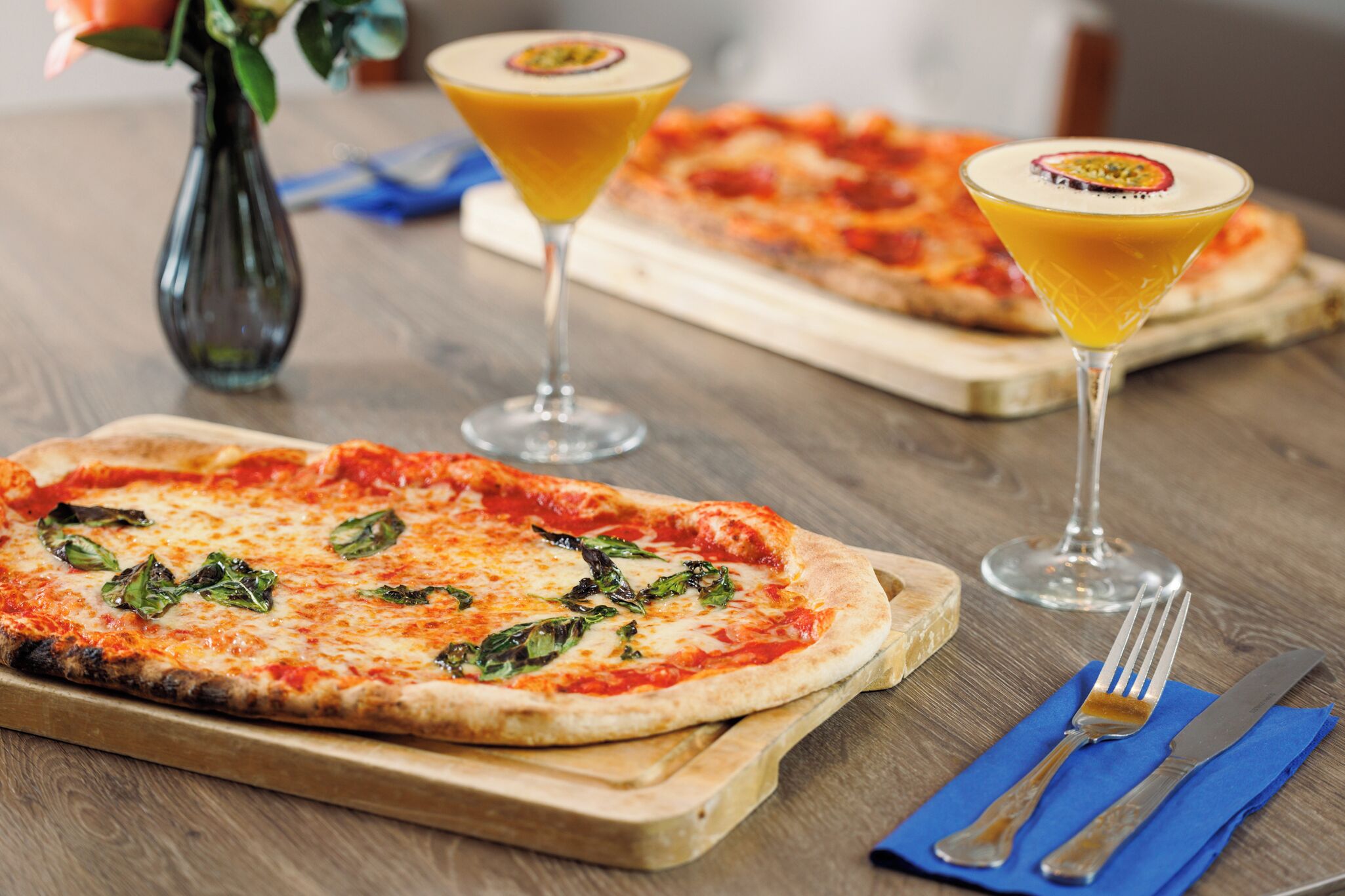 A wooden table with two pizzas and two martini glasses.