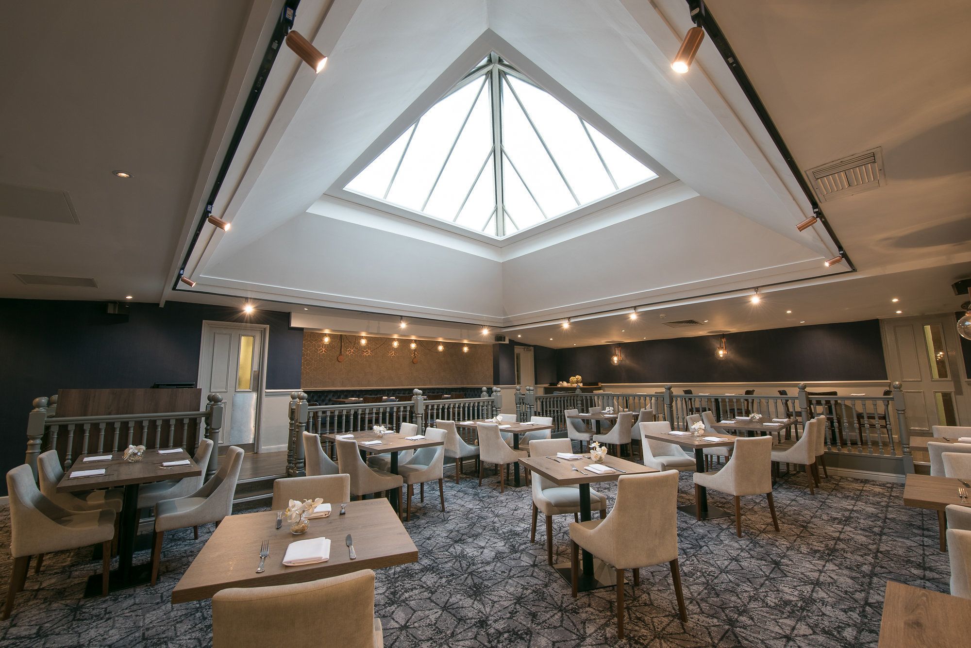 Een ruim restaurant met hoge plafonds en dakramen, met meerdere eettafels en stoelen.