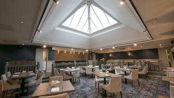 Een ruim restaurant met hoge plafonds en dakramen, met meerdere eettafels en stoelen.