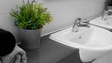 Un baño con un lavamanos blanco, un espejo y una planta en maceta.