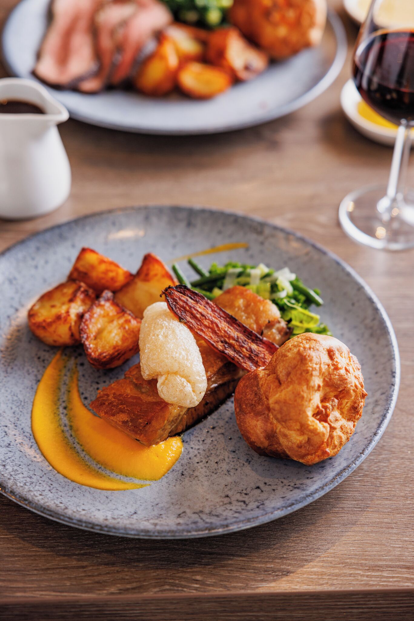 A plate of food with roasted potatoes, a piece of meat, and a pastry on a speckled ceramic plate.