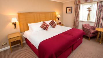 Ein Hotelzimmer mit einem großen Bett, zwei Nachttischen, einem Sessel und einem Fenster mit Vorhängen.