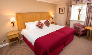 A hotel room with a large bed, two bedside tables, a chair, and a window with curtains.