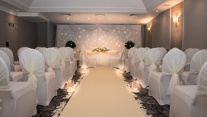 Un pasillo nupcial con sillas blancas y un arreglo floral al final.