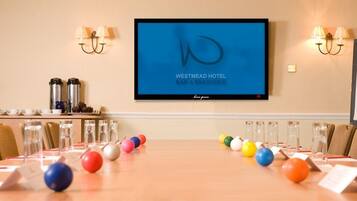 Un salón de conferencias con una larga mesa, sillas, una pantalla de televisión que muestra 'Westmead Hotel' y una pizarra con la palabra 'Signature' escrita.