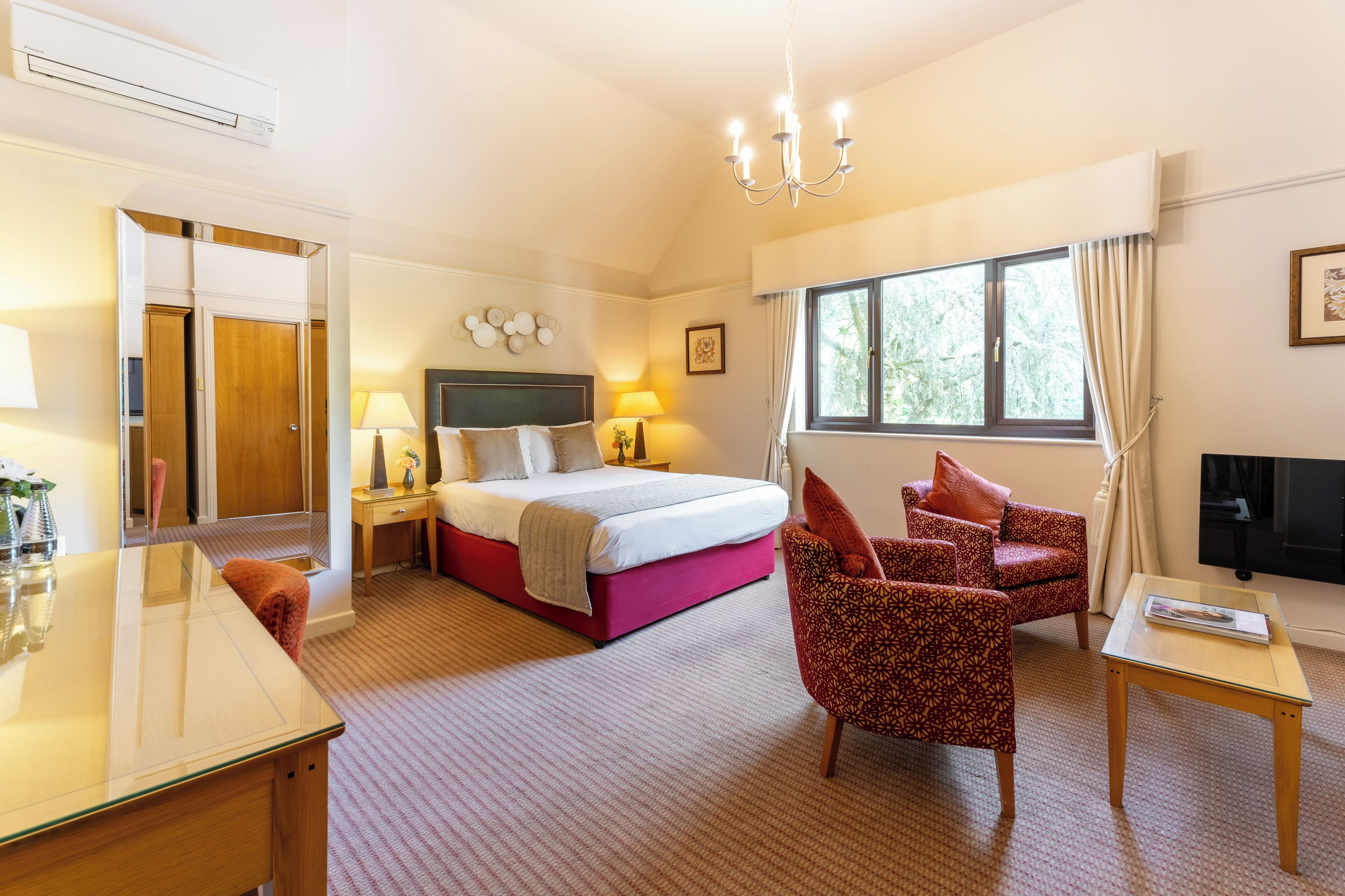 A hotel room with a bed, a desk, a chair, a TV, and a window with curtains.