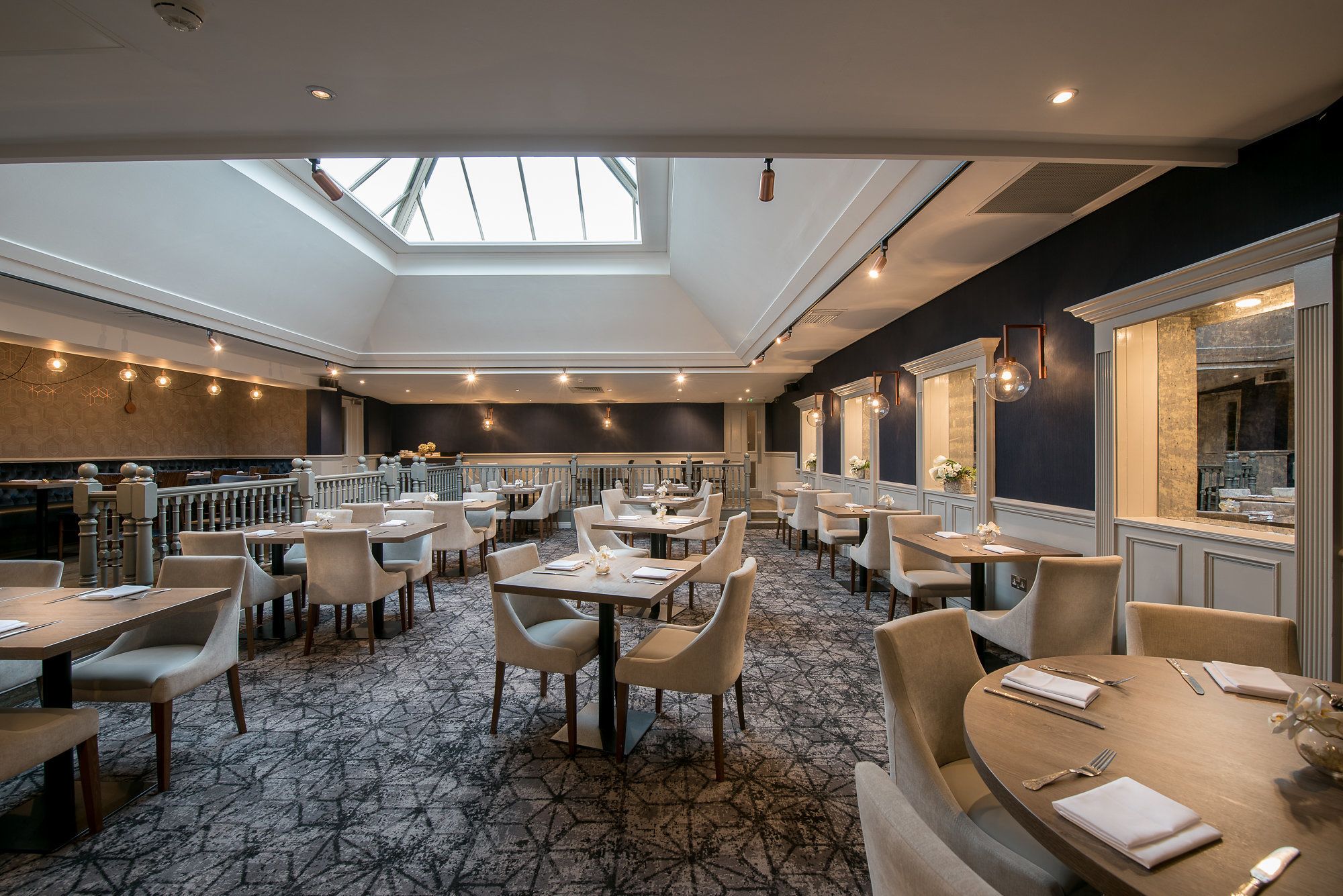 Ein geräumiges Restaurant mit hohen Decken und Oberlichtern, das eine Mischung aus runden und rechteckigen Tischen sowie einen gemusterten Teppich bietet.