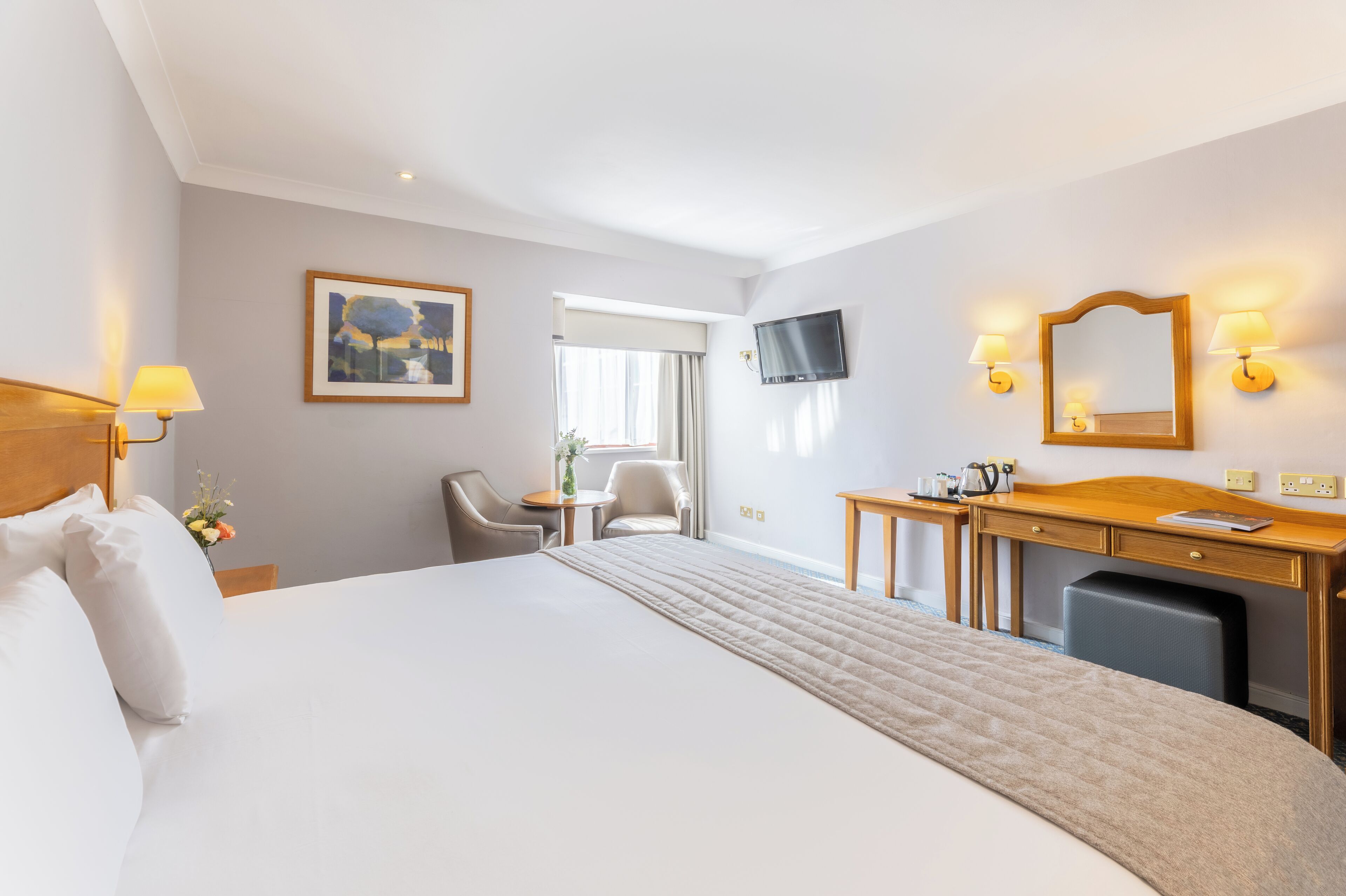 Habitación de hotel con una cama grande, un escritorio con una silla, un televisor y una ventana con cortinas.