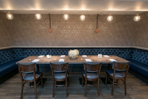 A dining area with a long table set for six, surrounded by blue upholstered booths, and overhead lighting.