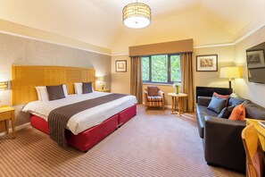 A hotel room with a large bed, a sofa, a small table, and a window with curtains.