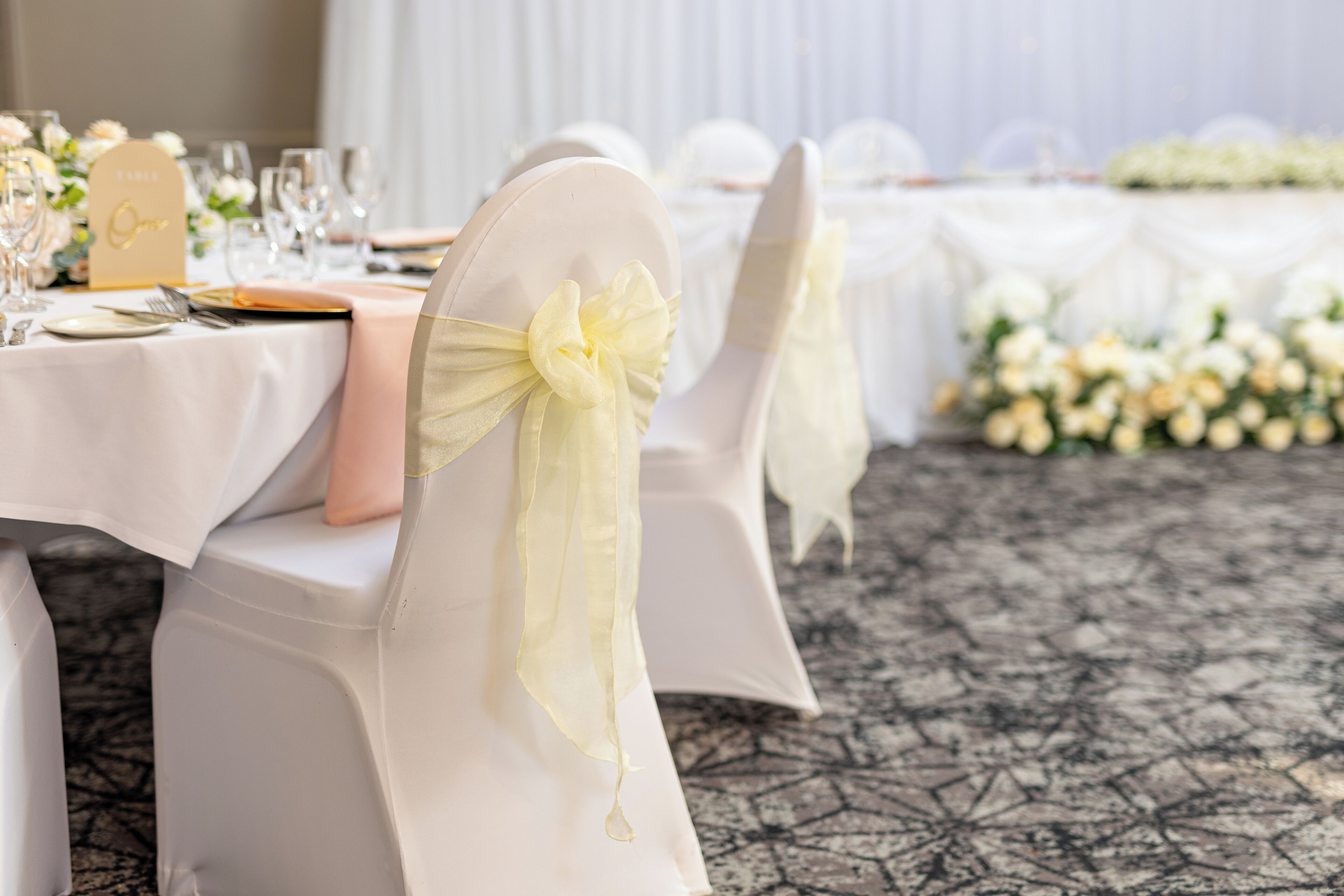 A table set with white tablecloths, gold name cards, and white flowers.