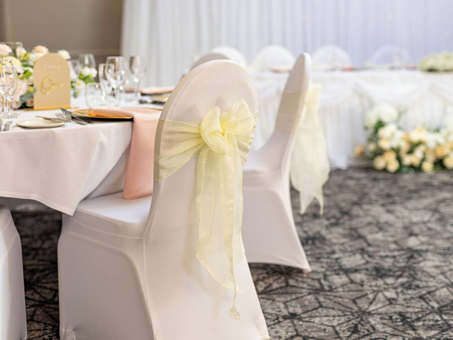Une table dressée avec des nappes blanches, des marque-places dorés et des fleurs blanches.