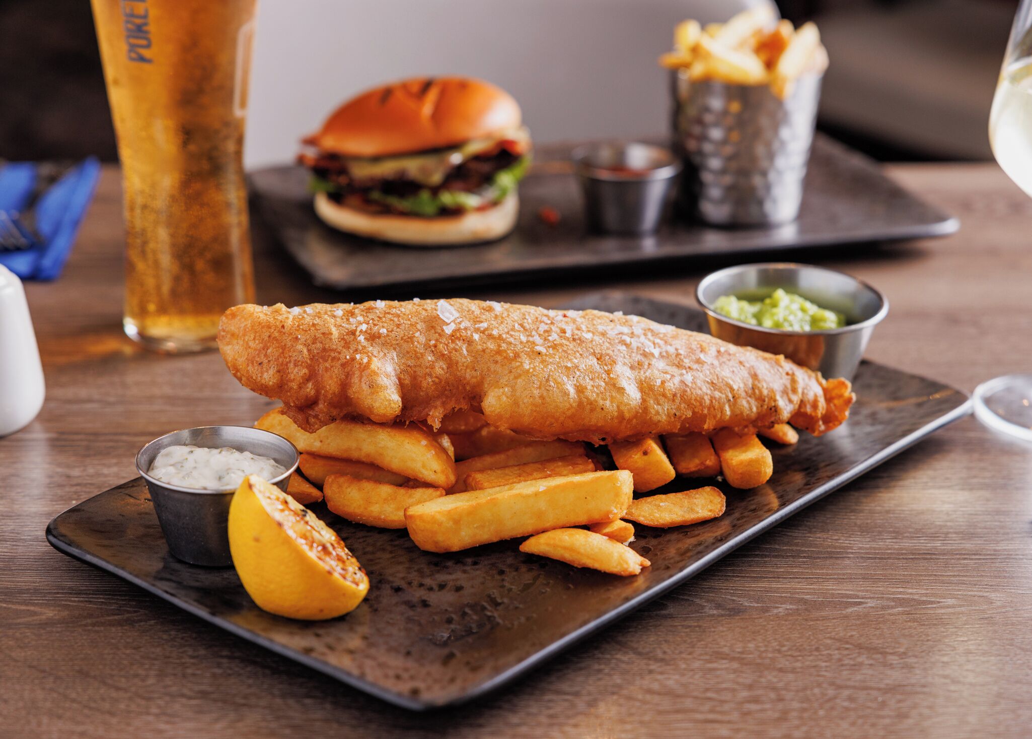 A meal of fish and chips with a burger and fries on a wooden table.