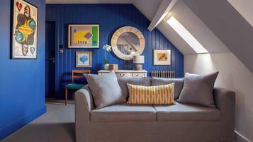 Una habitación acogedora con un muro azul de acento, un sofá gris con cojines estampados y un espejo con marco de madera.
