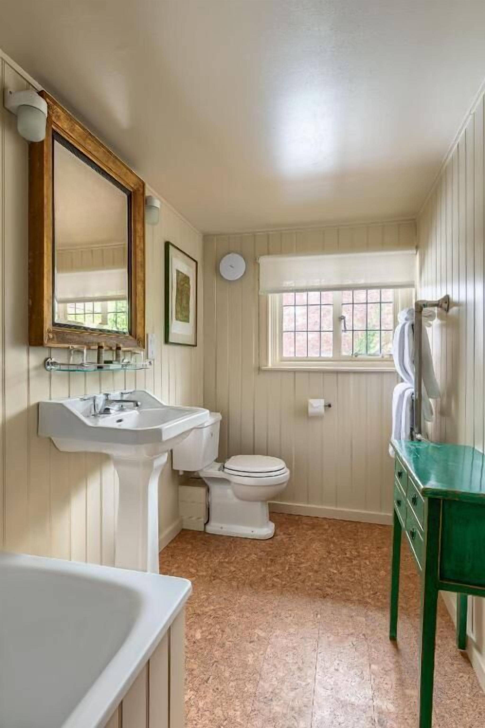 A bathroom with a white sink, toilet, and bathtub. There is a window with a view of greenery outside.