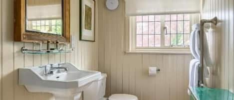 A bathroom with a white sink, toilet, and bathtub. There is a window with a view of greenery outside.