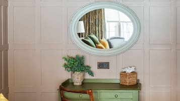 Quarto com escrivaninha verde, cadeira, cama e um espelho oval grande na parede.