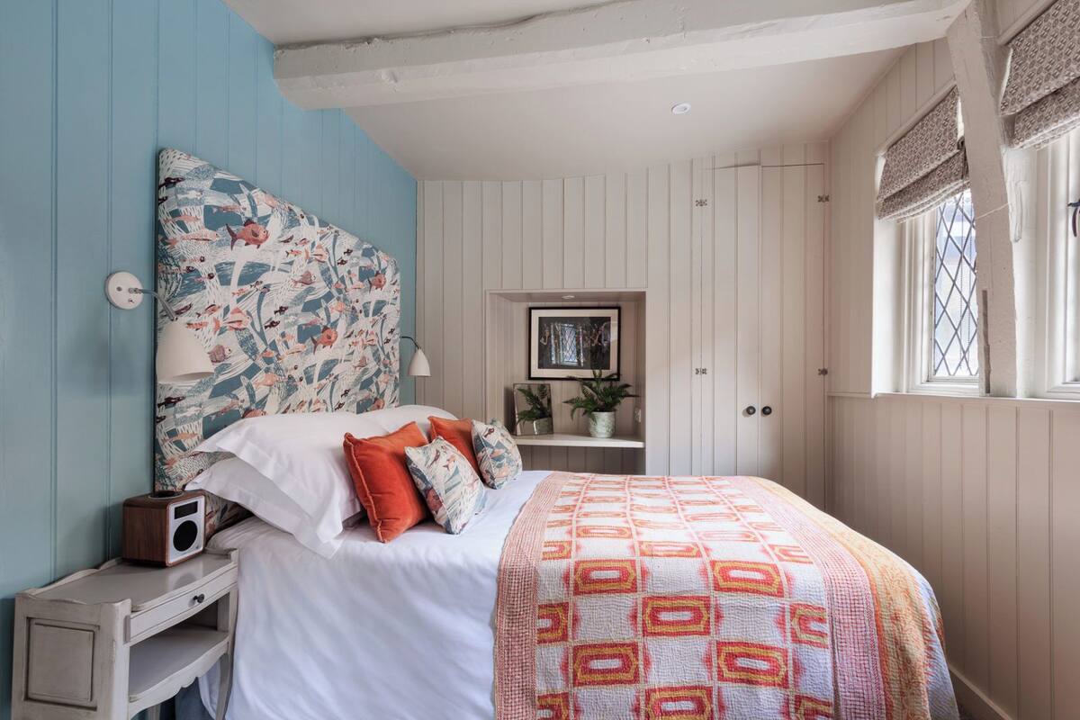 A bedroom with a bed, a nightstand, a lamp, and a window with shutters.