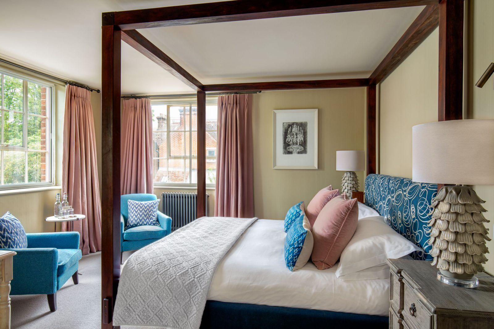 Una camera da letto con un letto a baldacchino, una poltrona blu, un tavolino con bicchieri e una lampada.