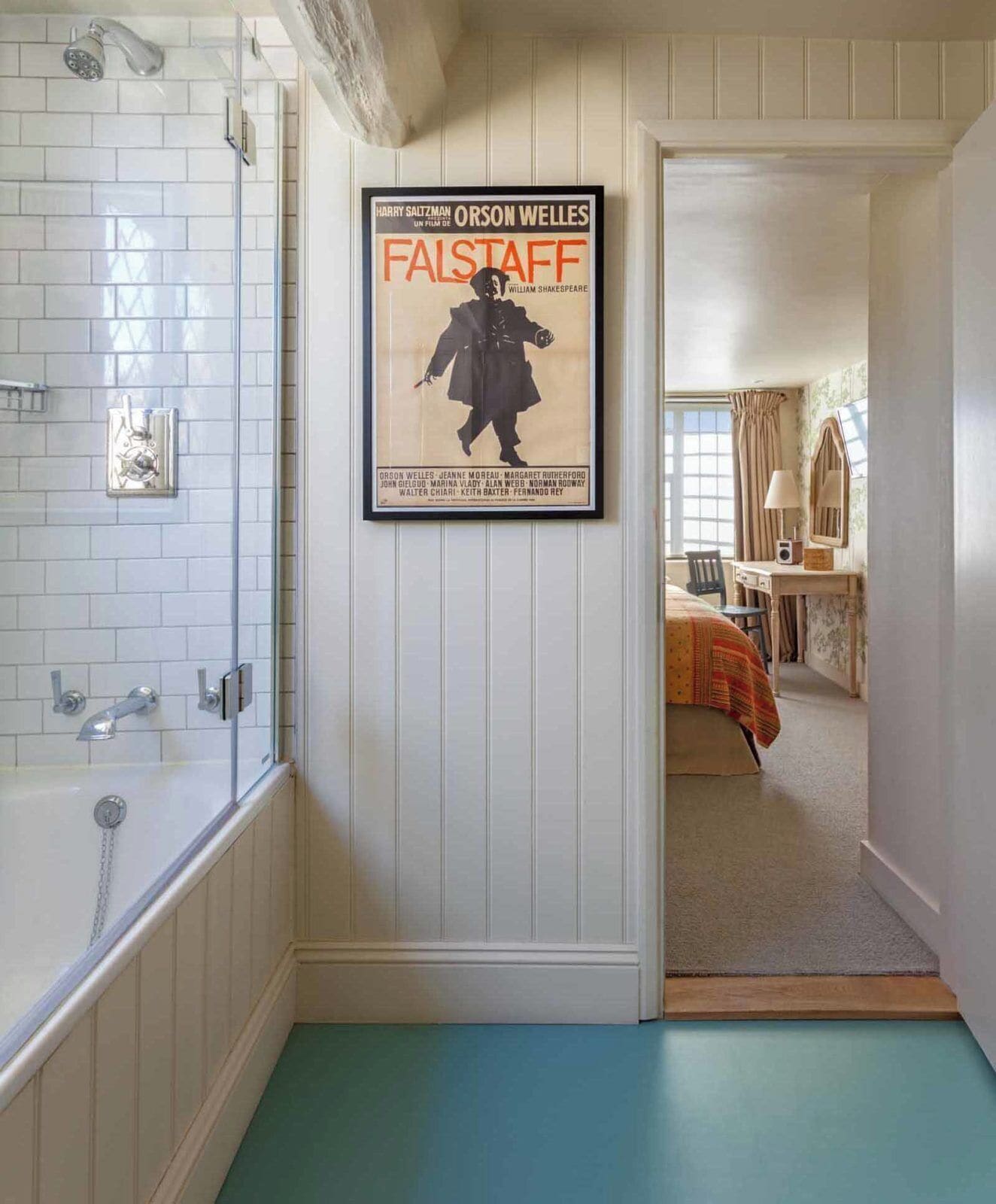 A bathroom with a shower, a poster of 'Falstaff' on the wall, and a view into a bedroom with a bed and dresser.