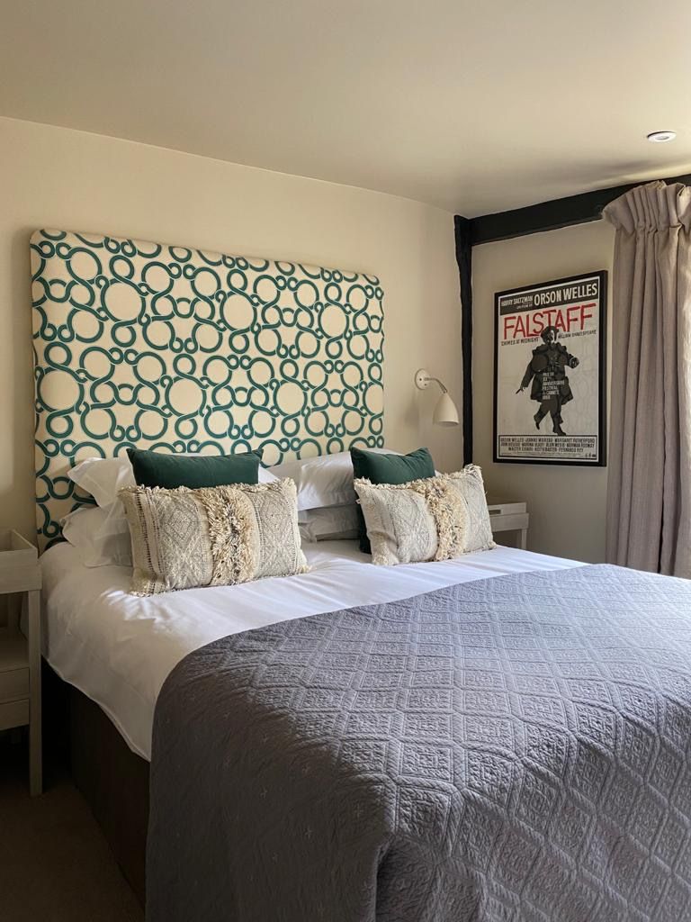 A hotel room with a large bed, a headboard with a circular pattern, two bedside tables with lamps, and a poster on the wall.