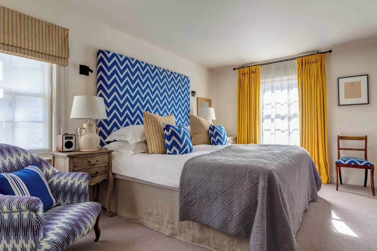 A hotel room with a large bed, a bedside table with a lamp, a chair, and a window with curtains.