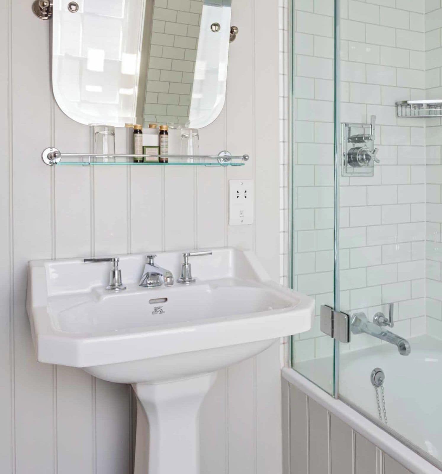 Un bagno con un lavabo a piedistallo bianco, un box doccia in vetro e uno specchio sopra il lavabo.
