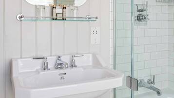 Un bagno con un lavabo a piedistallo bianco, un box doccia in vetro e uno specchio sopra il lavabo.