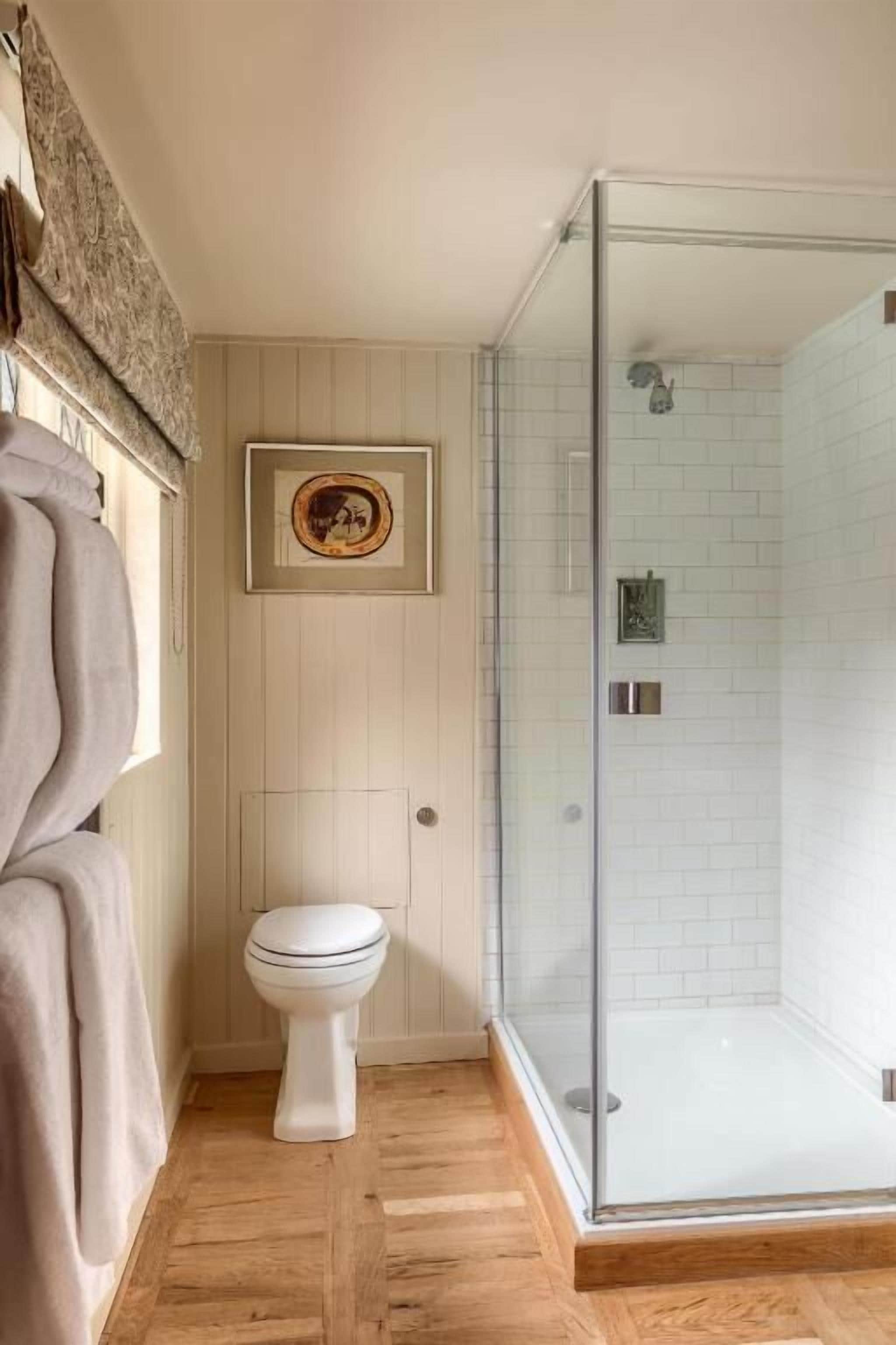 A bathroom with a glass-enclosed shower, a toilet, and a framed picture on the wall.