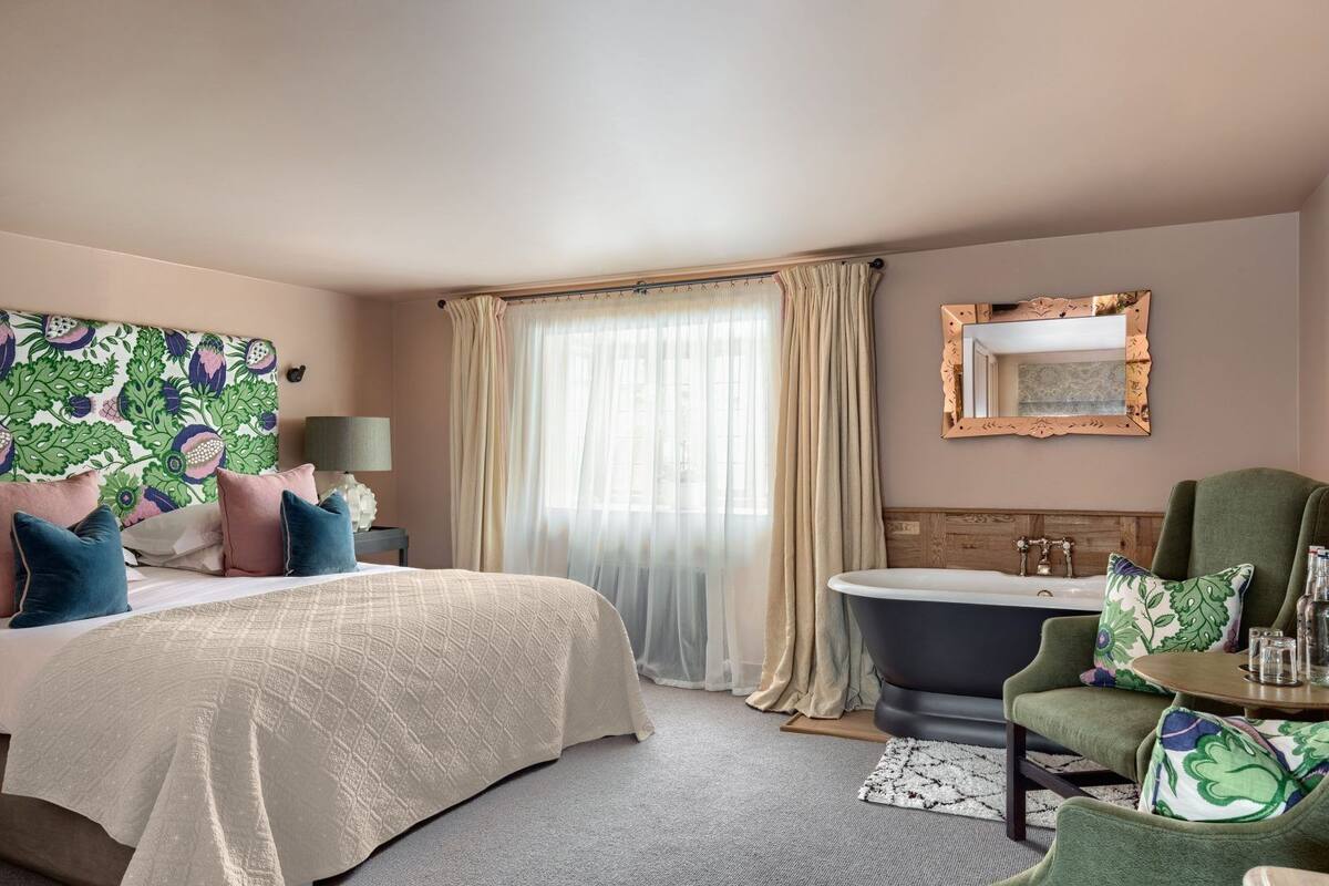 A bedroom with a bed, a green armchair, a bathtub, and a large mirror.