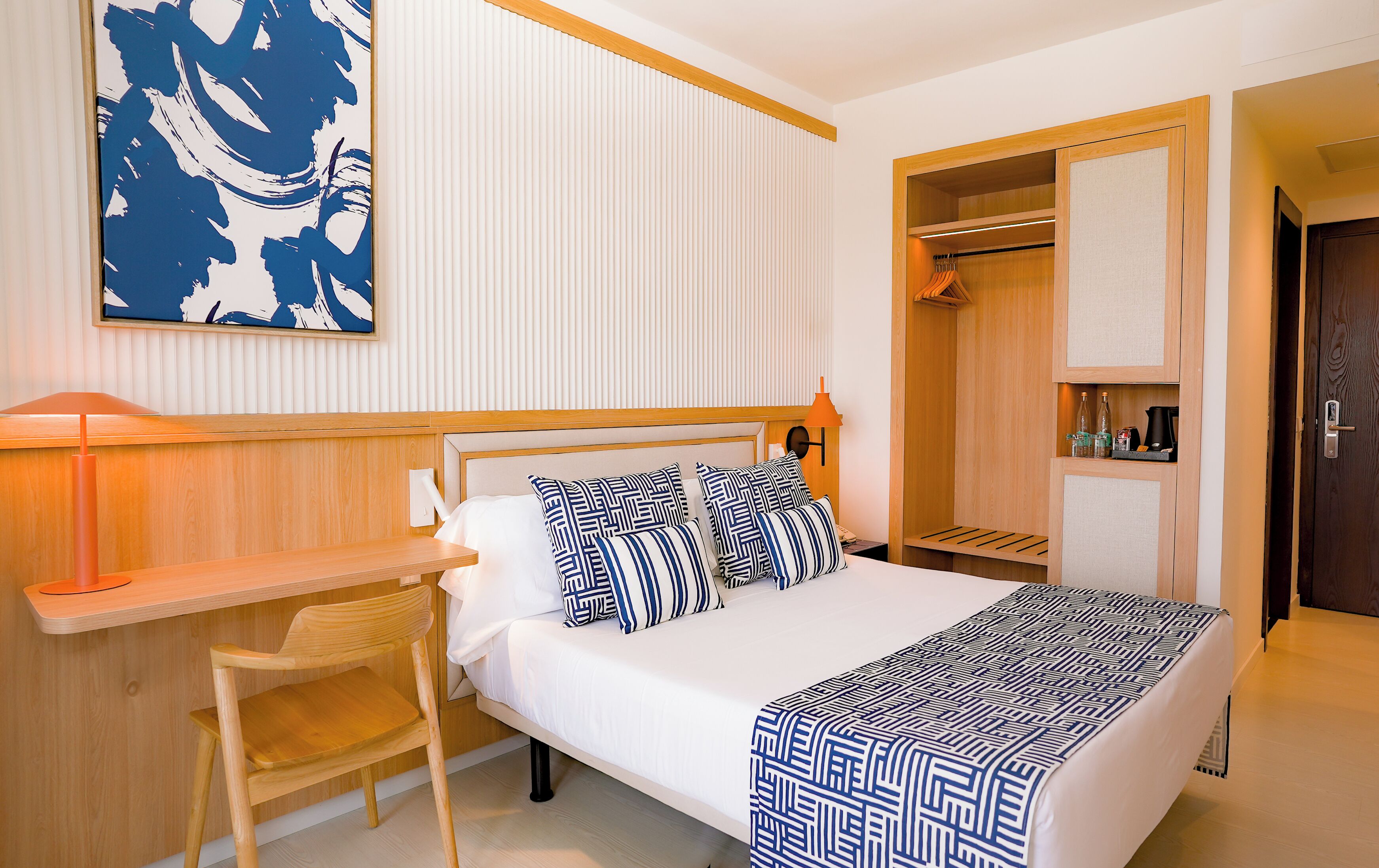 Een hotelkamer met een bed, nachtkastje, stoel en een garderobe met spiegel.