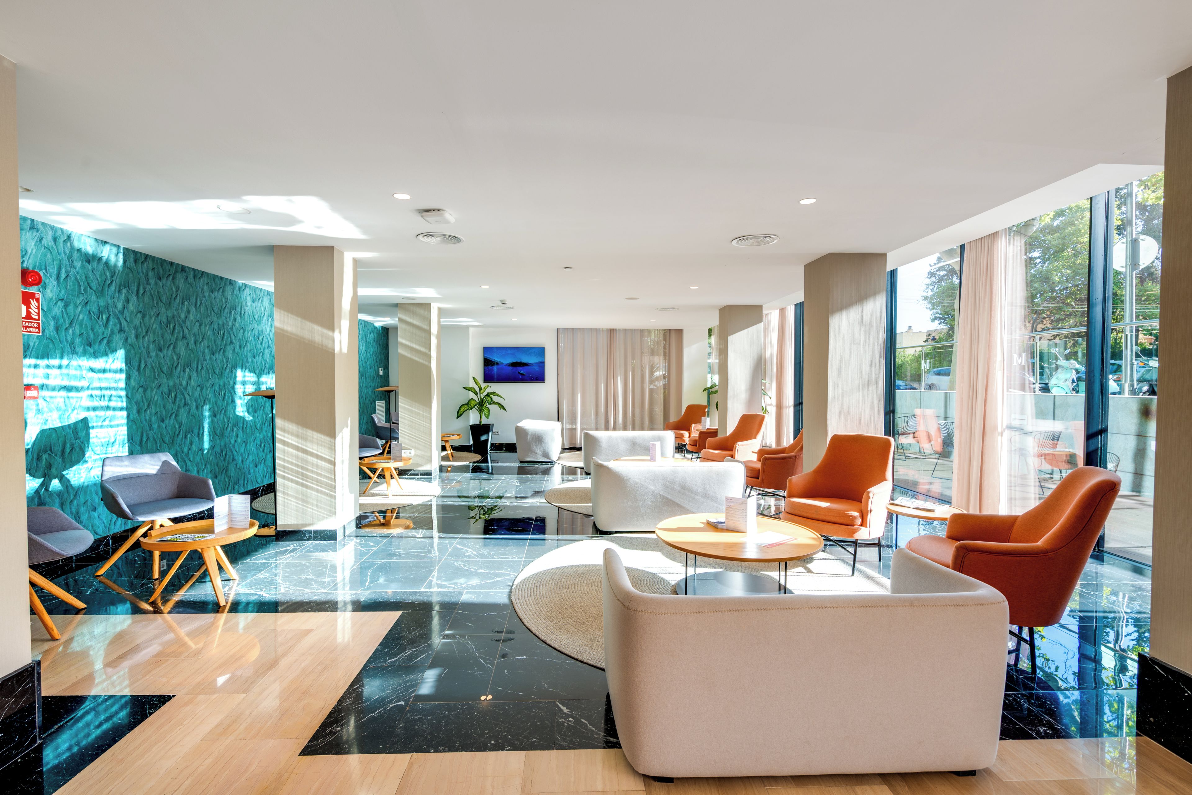 Een moderne hotel lobby met een zithoek, een flatscreen televisie en grote ramen.