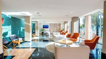 Een moderne hotel lobby met een zithoek, een flatscreen televisie en grote ramen.