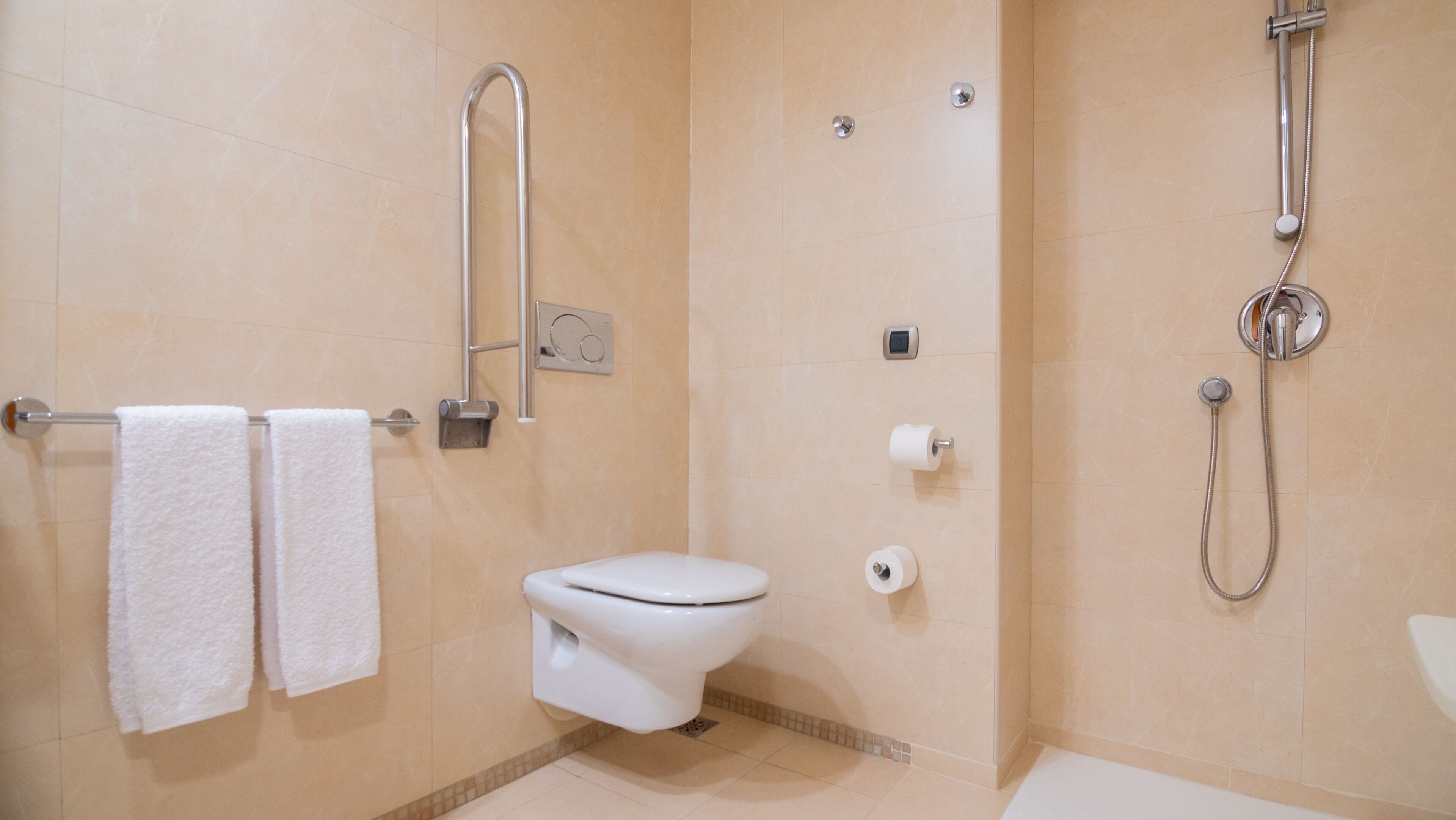 A modern bathroom with a toilet, a handrail, a shower, and two towels on a rack.