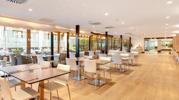 A modern restaurant with multiple dining tables and chairs, large windows, and a polished wooden floor.